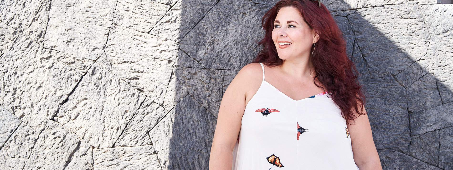 A woman standing in front of a rocky wall smiling and looking to the left.