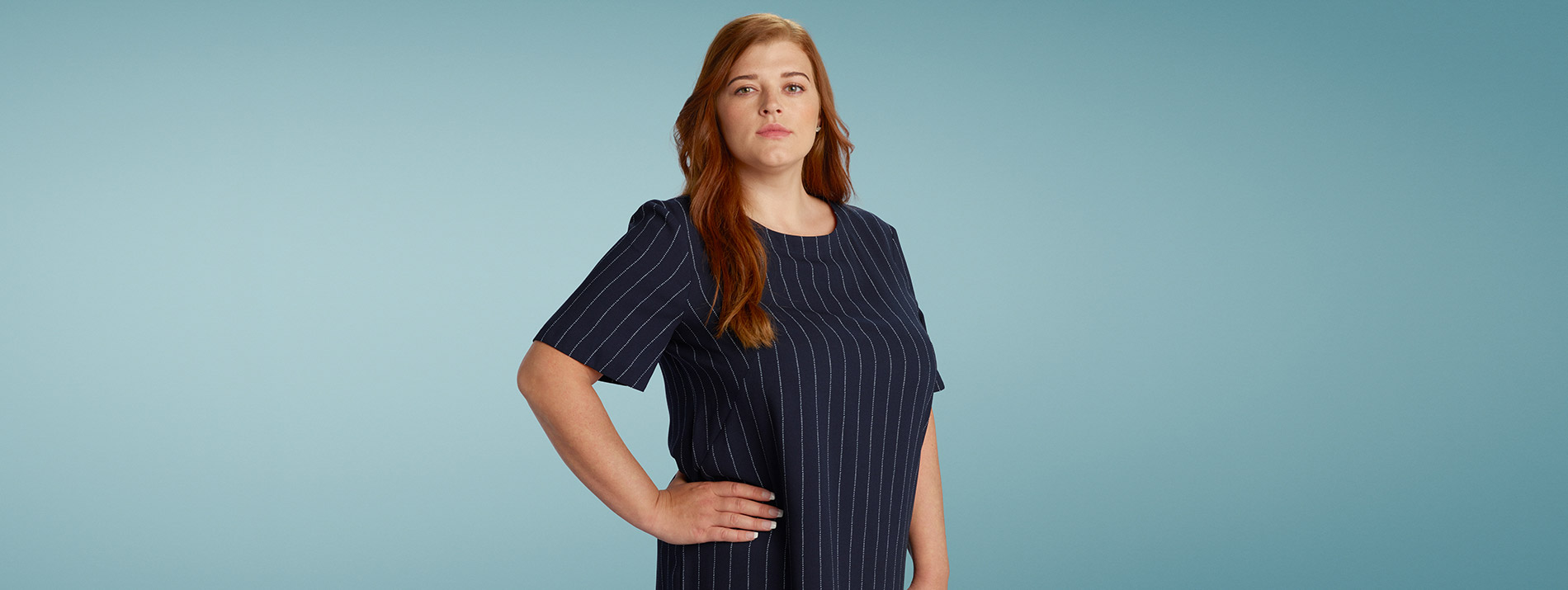 Right-aligned portrait of a confident looking woman in a striped blue dress.
