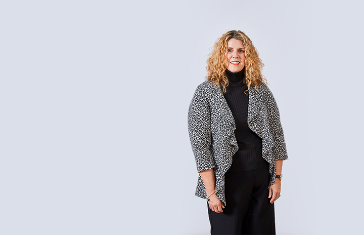 Curly-haired woman in a black dress with a spotted cardigan on top.