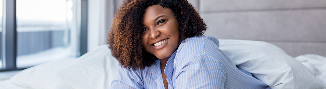 Woman in the blue blouse in the white covers, lying on the bed and smiling