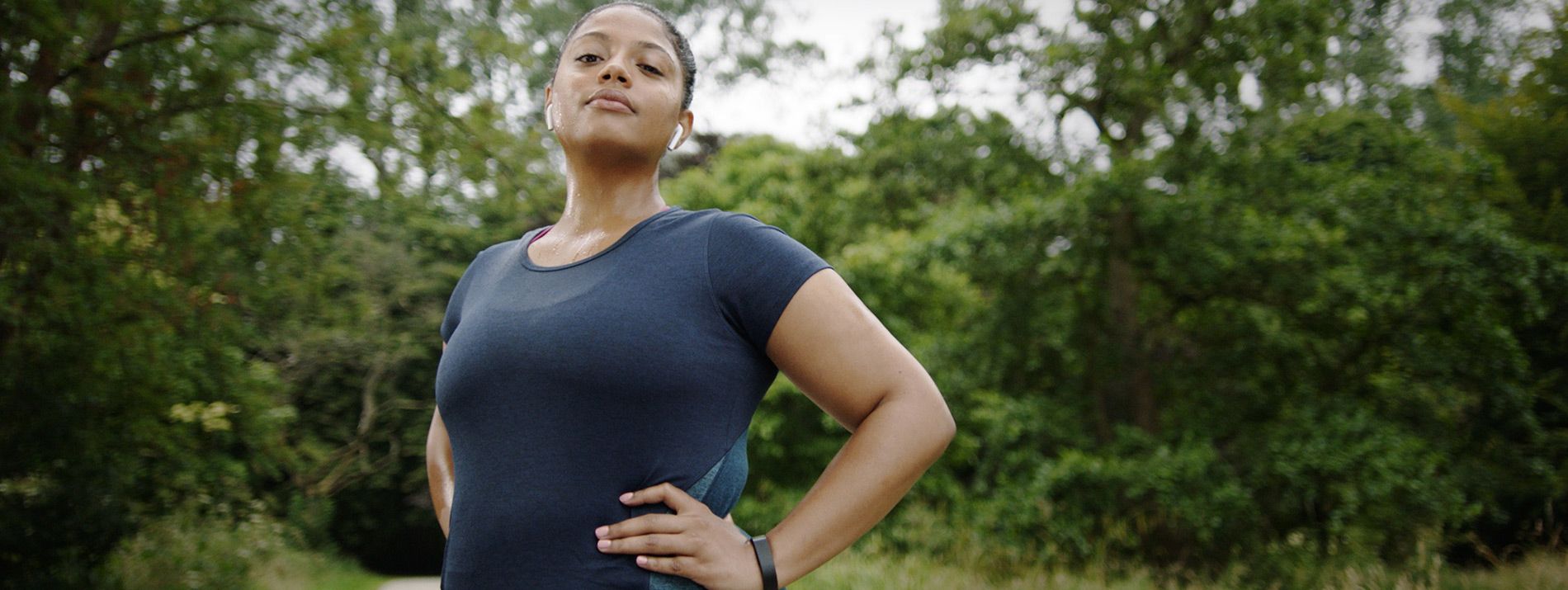 A centered view of a confident looking woman standing in front of a forest.